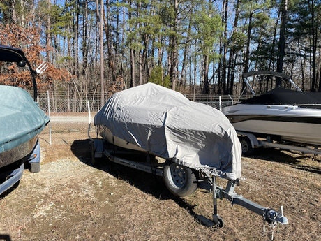 A boat sitting on a trailer with a grey winter cover